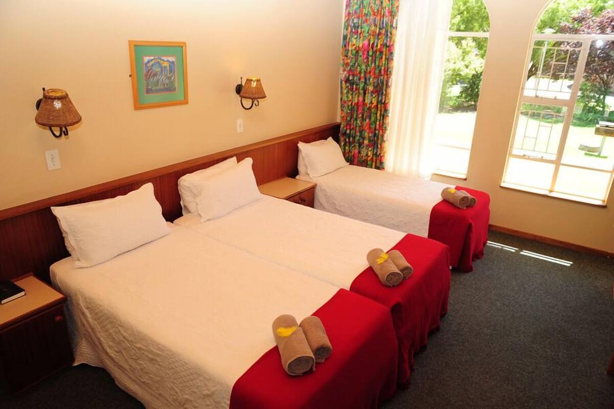 A hotel room with two beds, a window with a view, and a lamp on the wall.