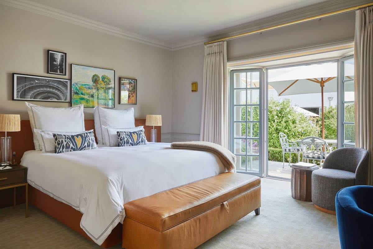 A hotel room with a large bed, a bench, a chair, a table, and a view of the outdoors.