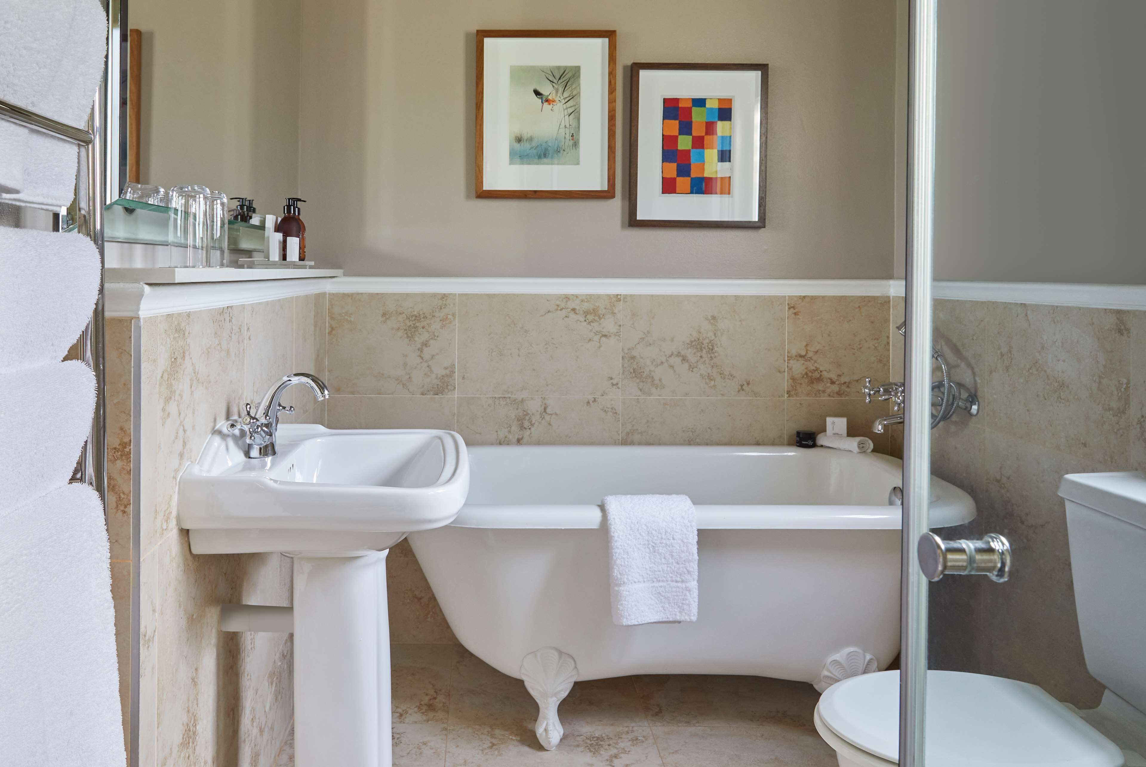 A bathroom with a white bathtub, a sink, and a toilet. There are two framed pictures on the wall.