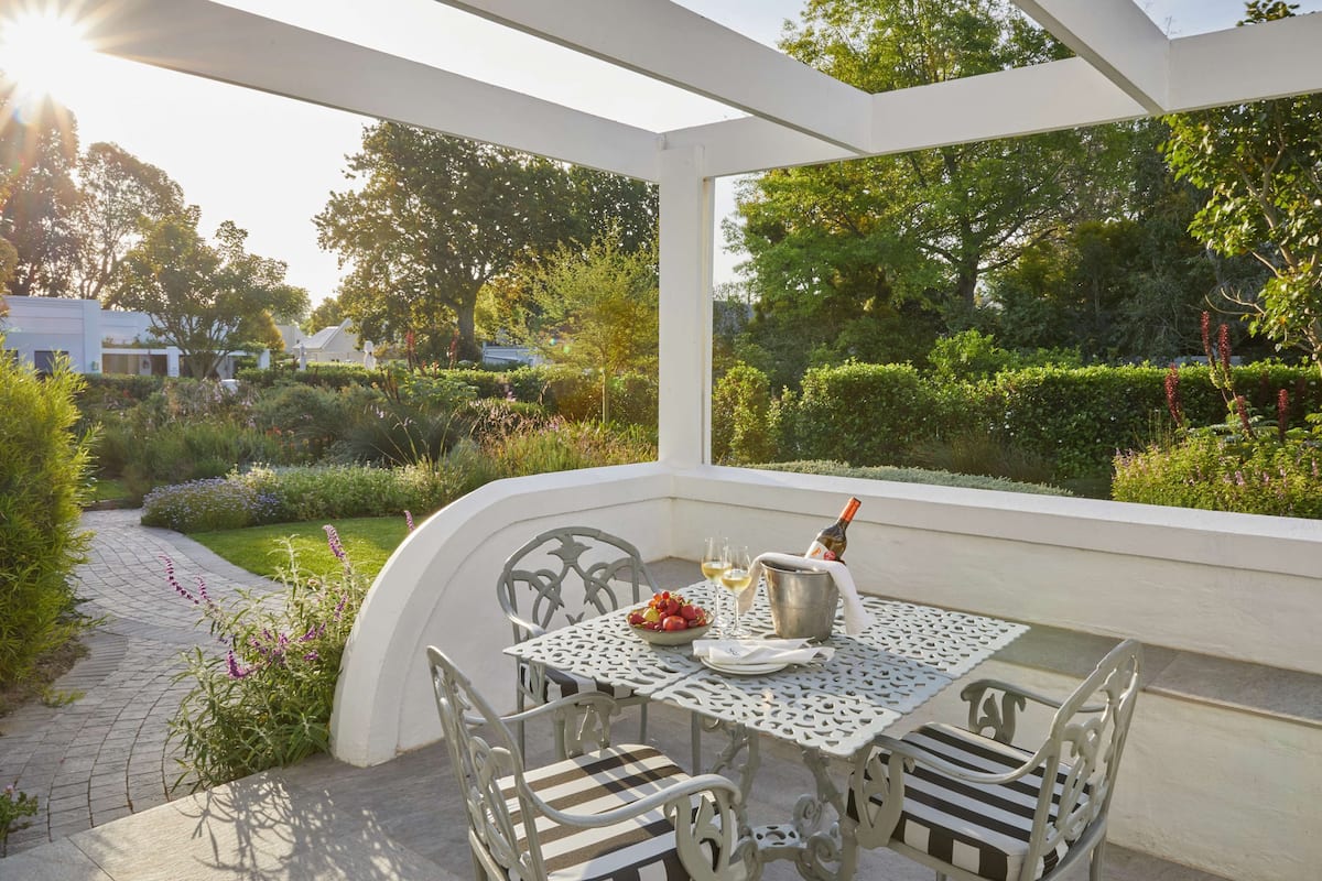 A covered patio with a table set for two, featuring a bottle of wine, glasses, and a bowl of fruit.