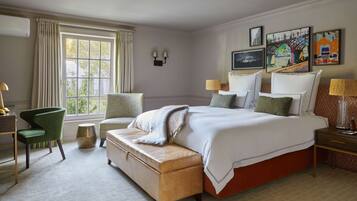 A hotel room with a large bed, two chairs, a bench, a desk, and a window with curtains.
