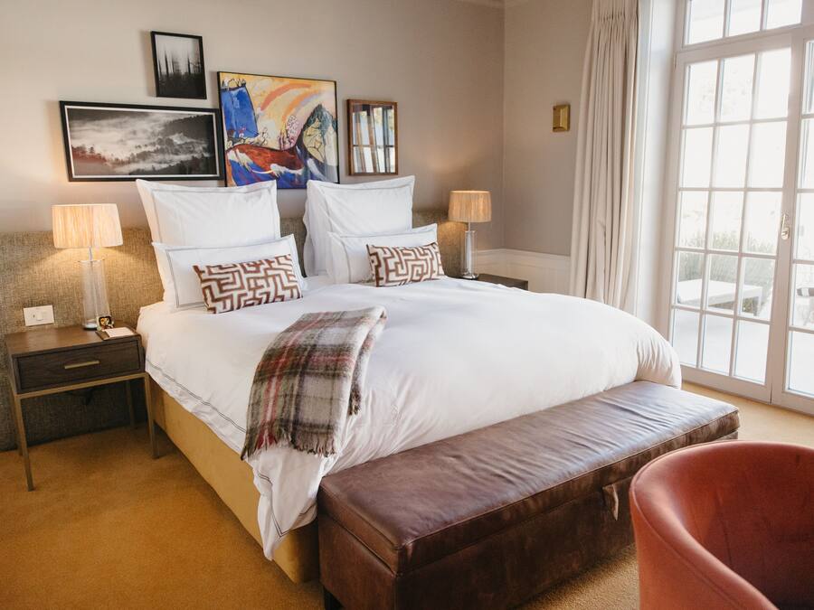 Un cuarto de hotel con una cama grande, dos mesitas de noche con lámparas, un banco y obras de arte en las paredes.