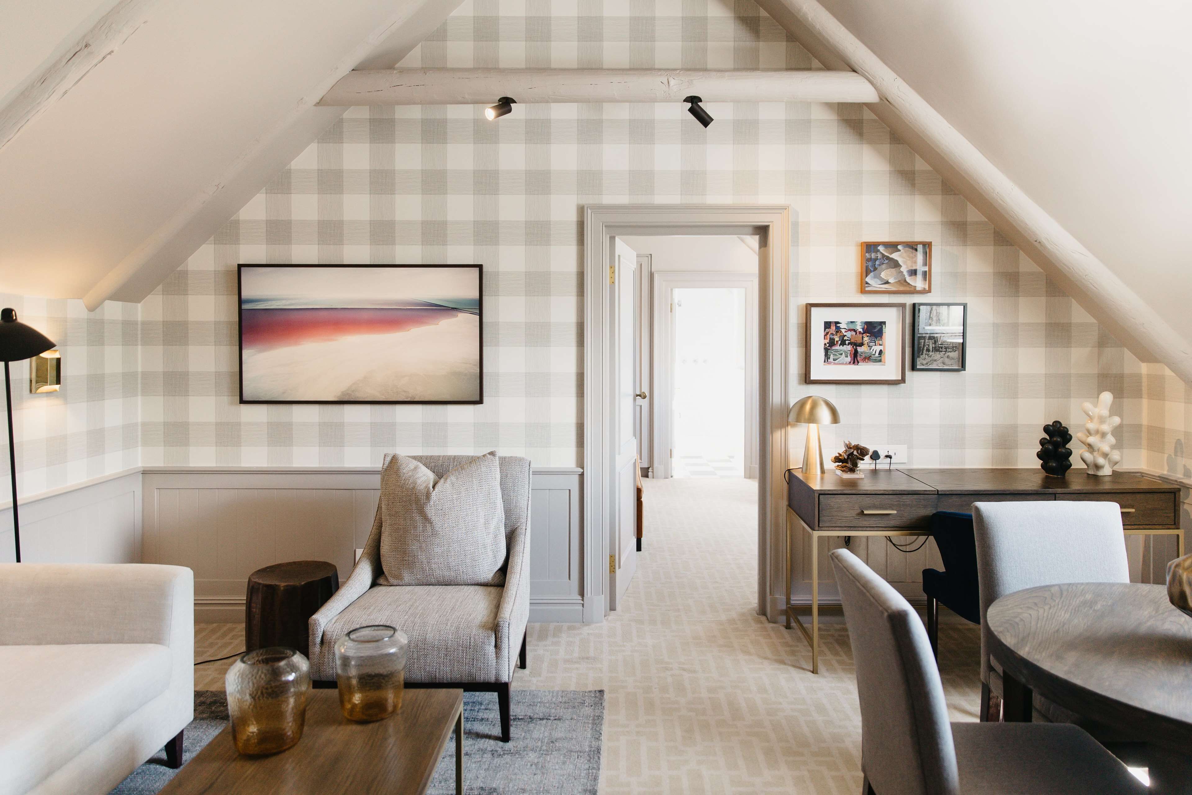 A cozy loft bedroom with a checkered wall, a large abstract painting, a desk with a lamp, and a dining area.