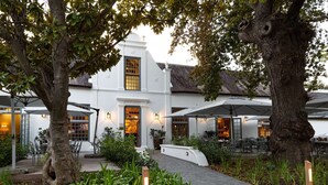A white building with a large entrance and multiple outdoor seating areas with umbrellas. - Erinvale Estate Hotel And Spa (Cape Town)