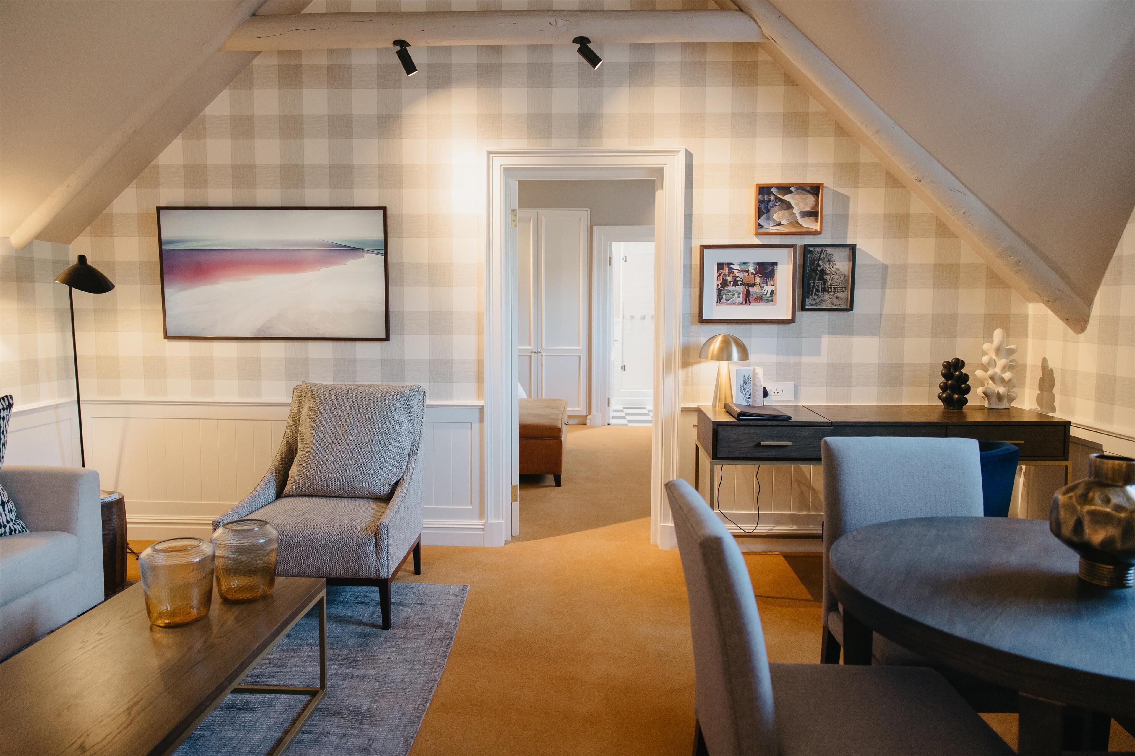 A cozy living room with a sofa, coffee table, and a dining area with chairs and a table. There is a kitchen area with a counter and a door leading to another room.