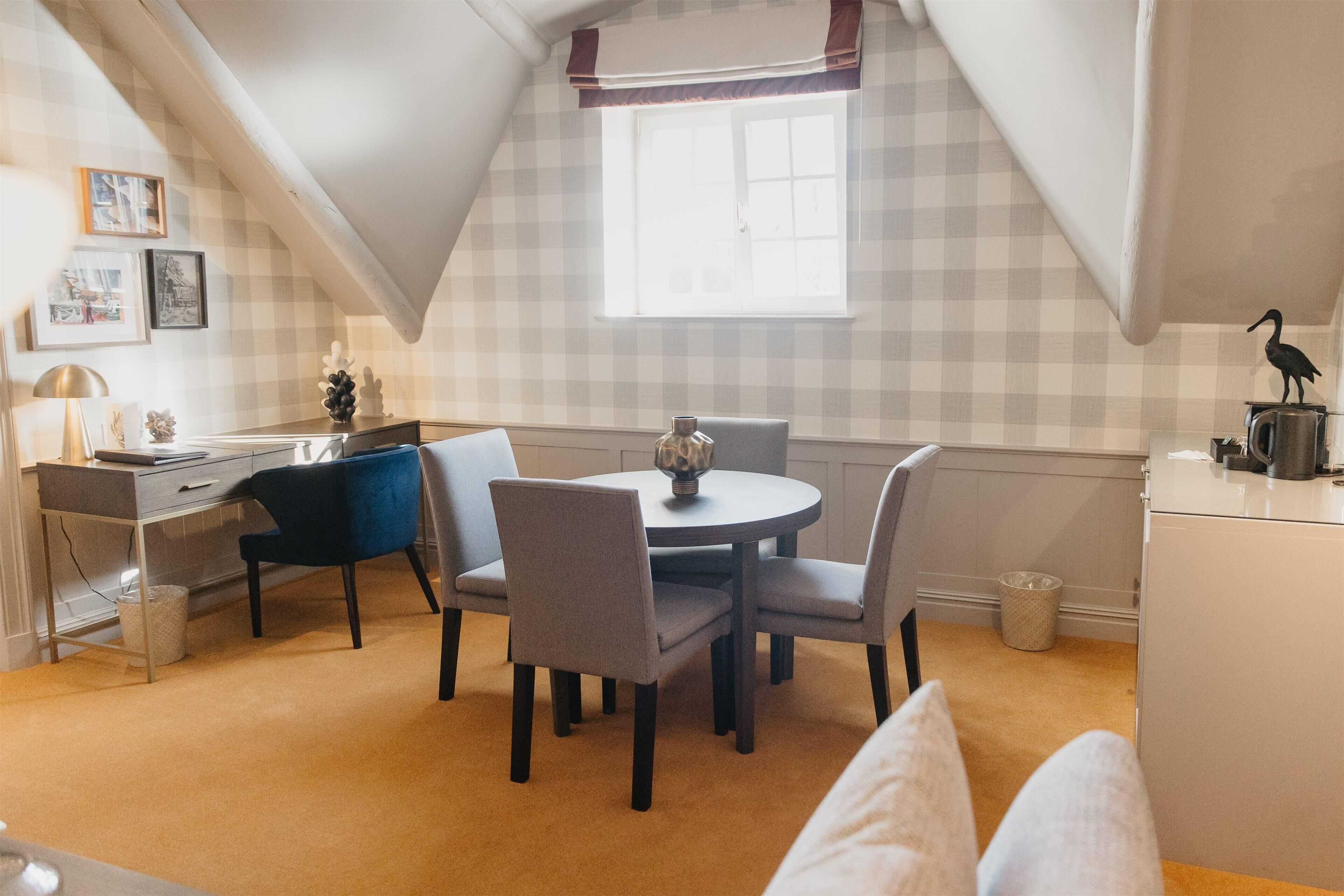 A cozy room with a dining table, chairs, a desk, and a window with a view.