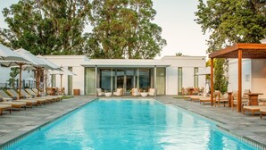 A swimming pool with lounge chairs and umbrellas, surrounded by trees and a modern building. - Erinvale Estate Hotel And Spa (Cape Town)