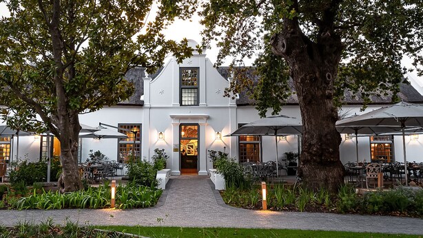 A white building with a central entrance, surrounded by outdoor seating areas and trees. - Erinvale Estate Hotel And Spa (Cape Town)