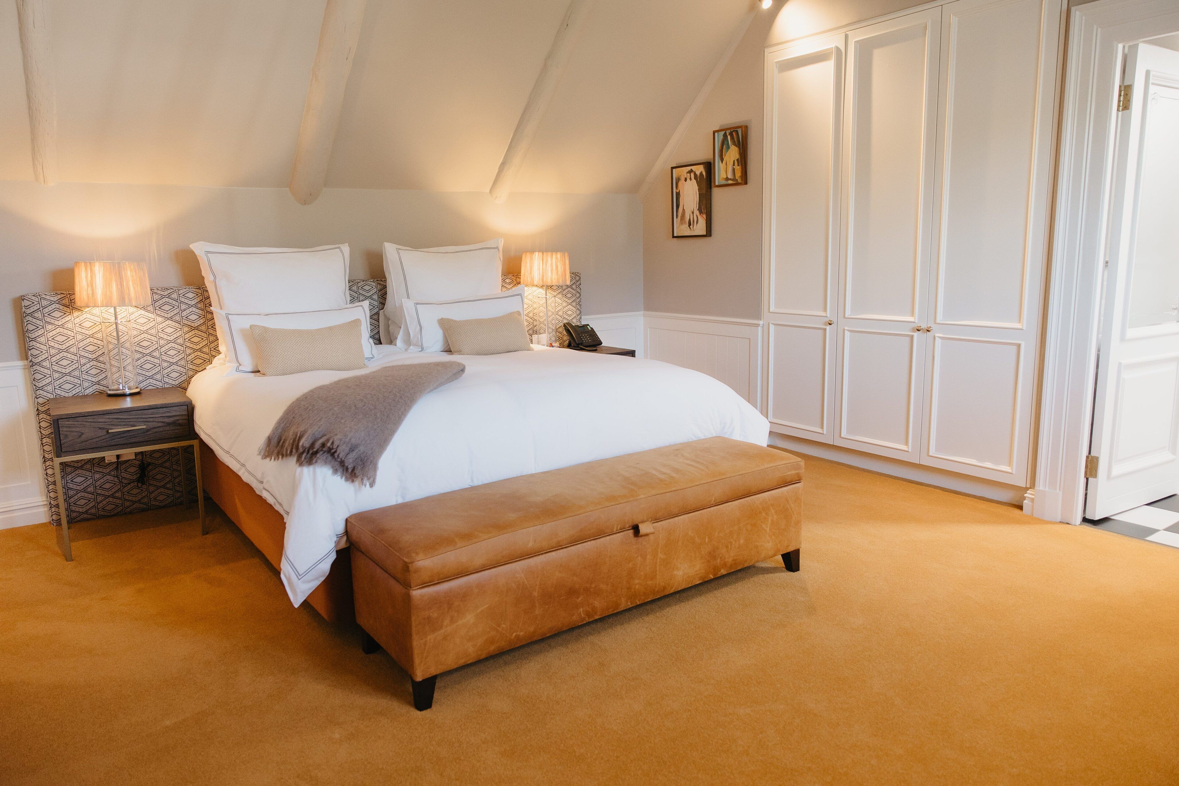 A bedroom with a large bed, bedside lamps, a bench, and a wardrobe.