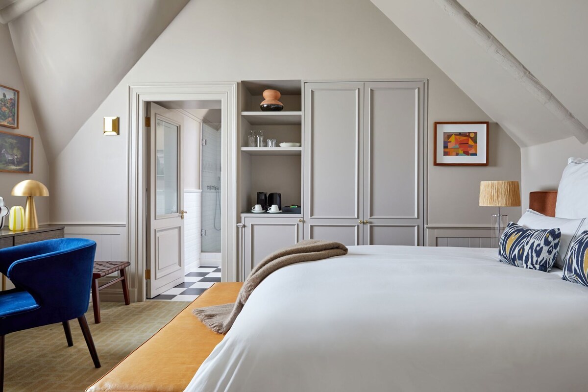 A bedroom with a bed, a desk, a chair, a wardrobe, and a bathroom with a shower.