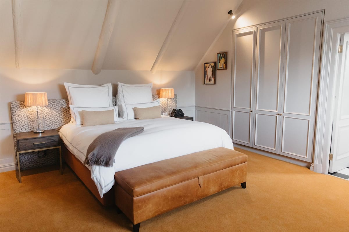 A bedroom with a large bed, two bedside tables, a wardrobe, and a carpeted floor.