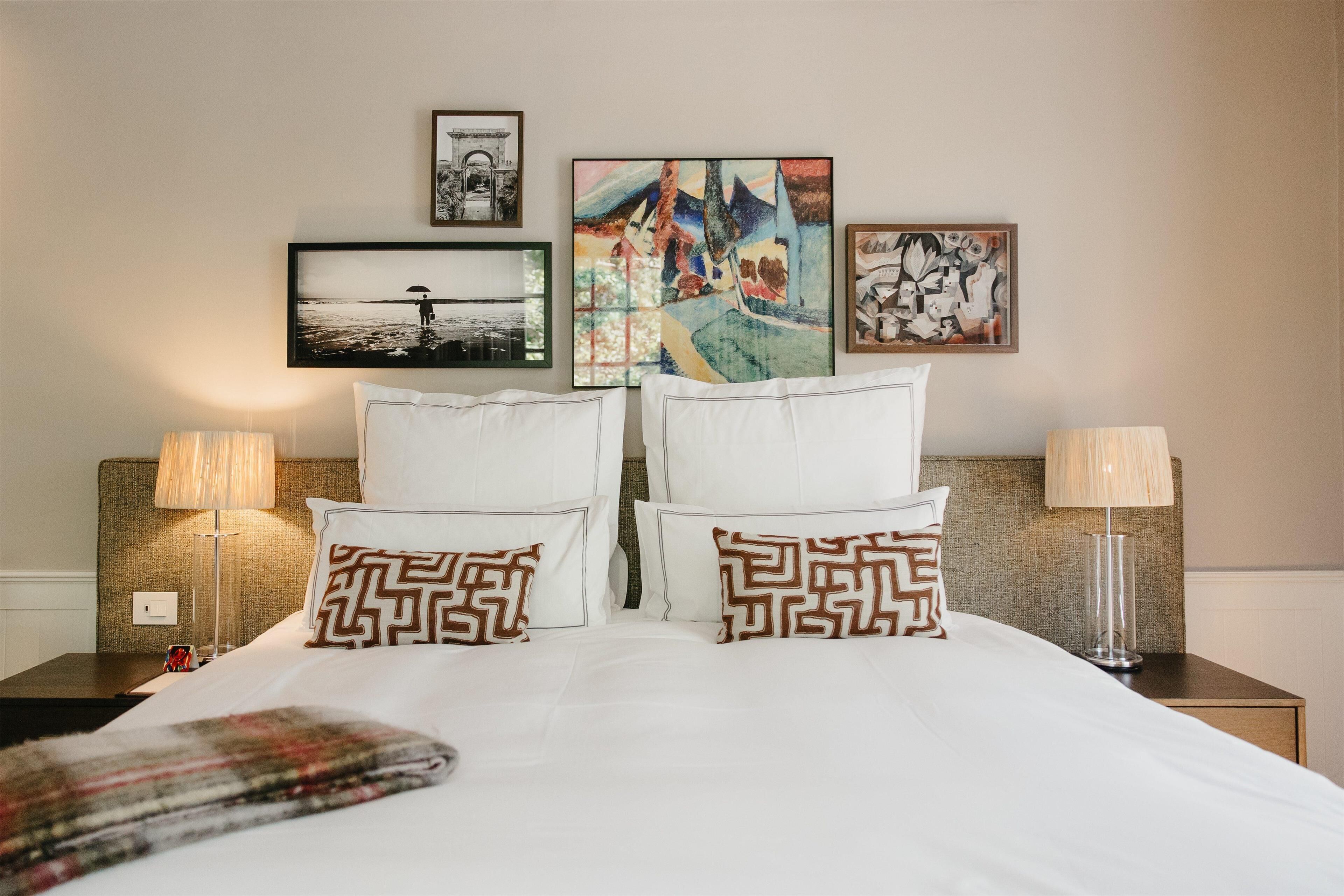 A neatly made bed with patterned pillows, two bedside lamps, and three framed artworks on the wall.