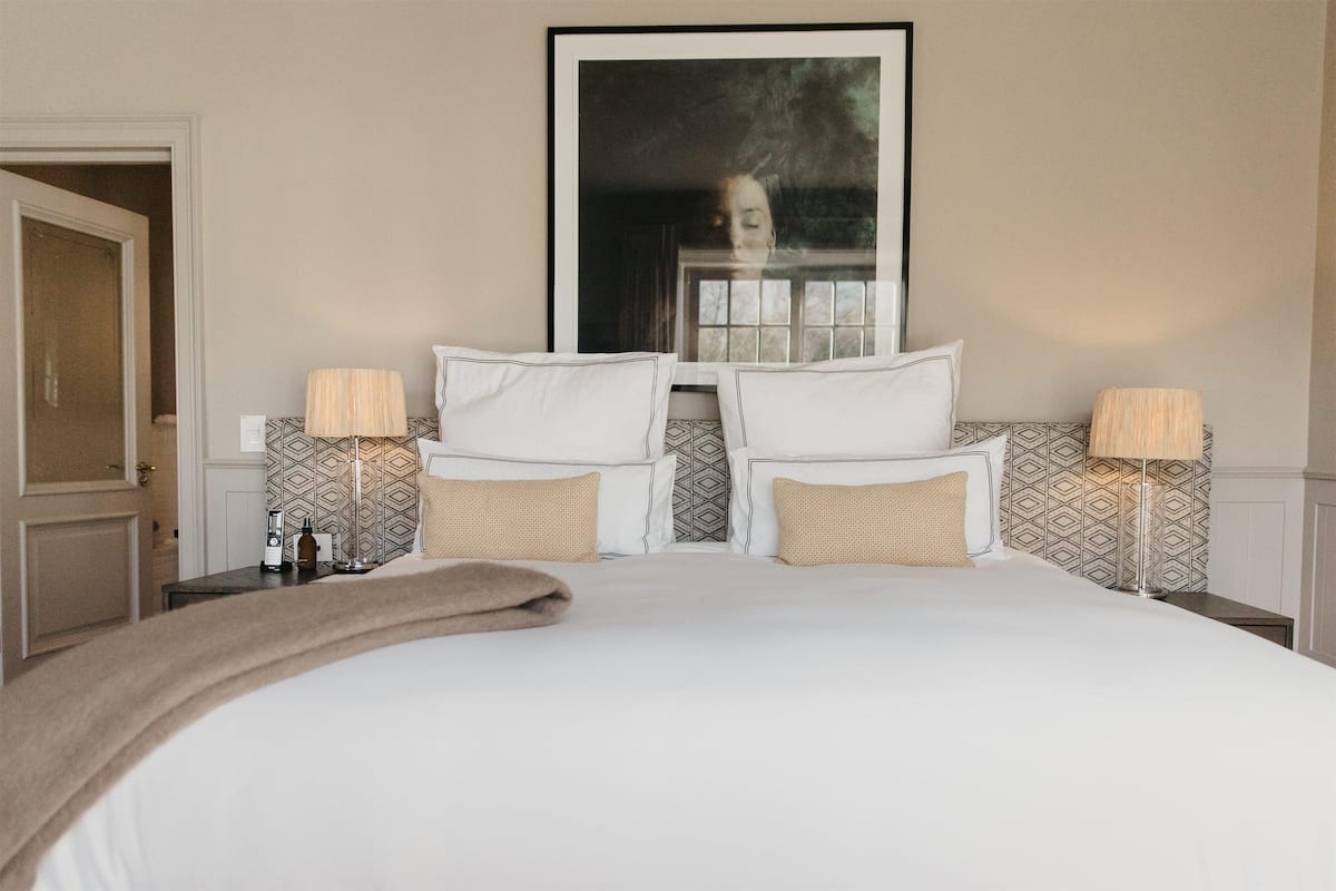 A hotel room with a large bed, two bedside tables with lamps, a framed picture on the wall, and patterned wallpaper.