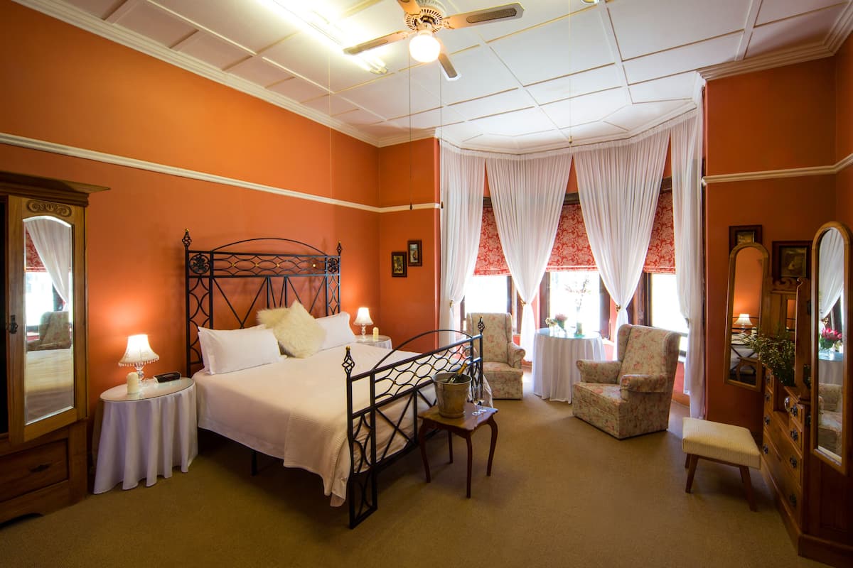 A hotel room with a bed, a chair, a table, a mirror, and curtains.