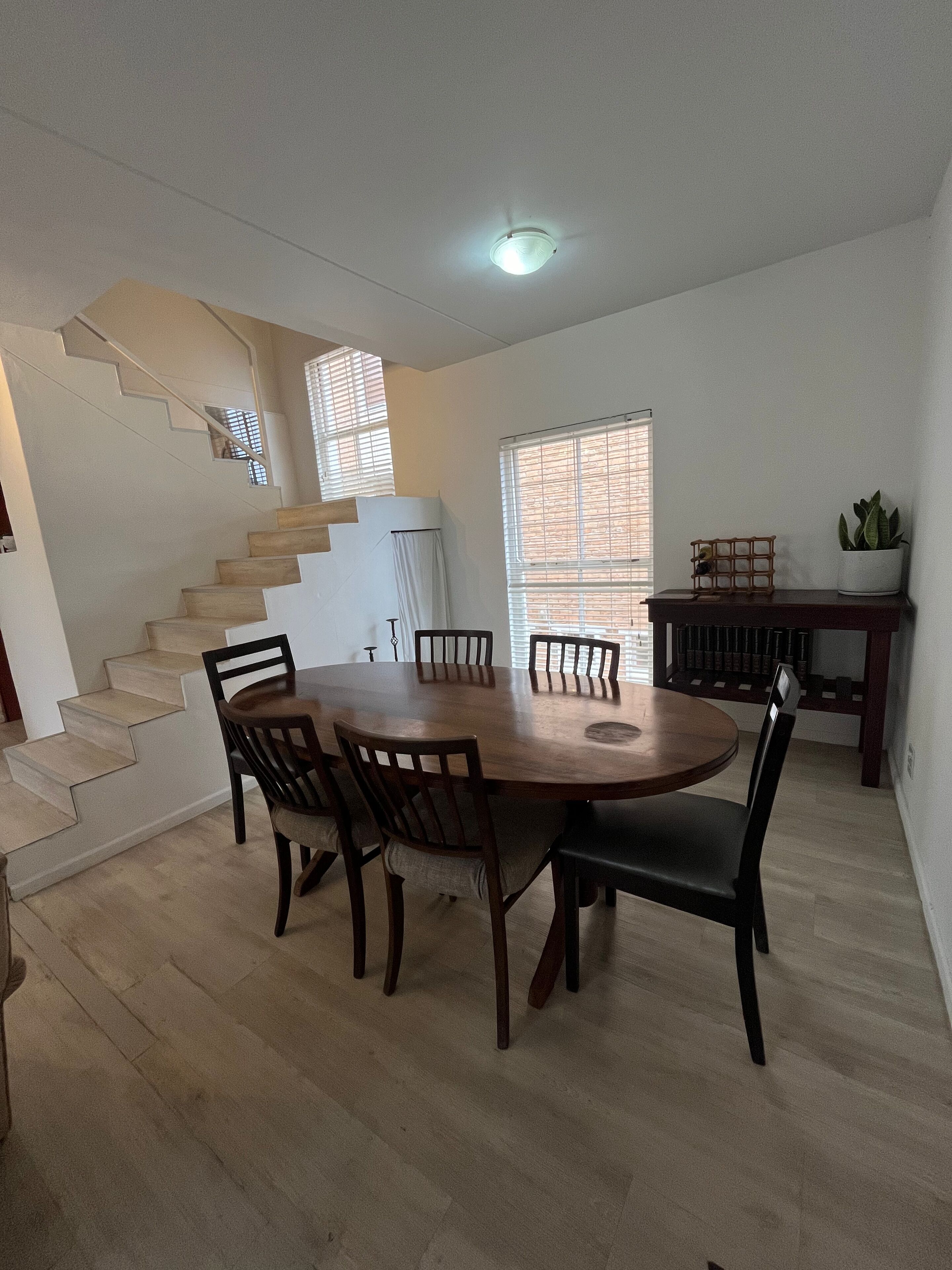 A dining area with a wooden table and chairs, a staircase, and a potted plant.