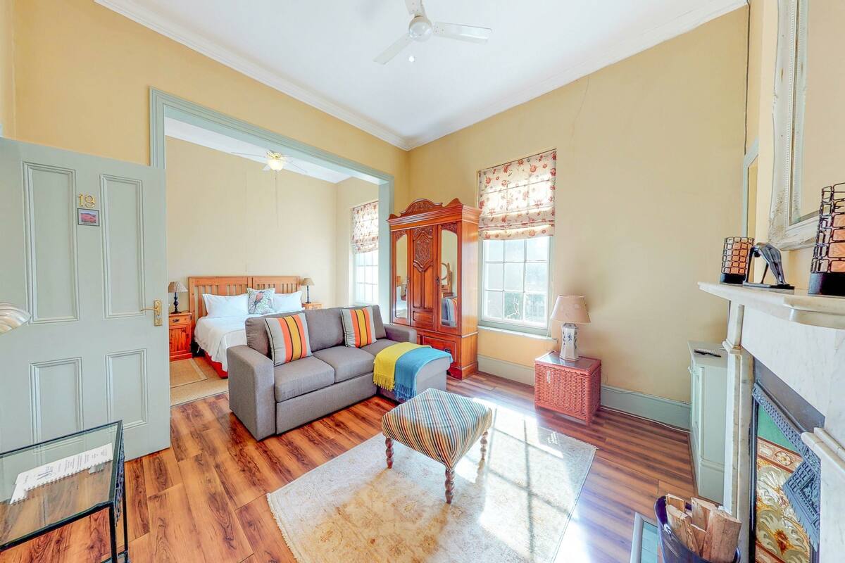 A spacious living room with hardwood floors, a grey sofa, a wooden cabinet, and a fireplace.