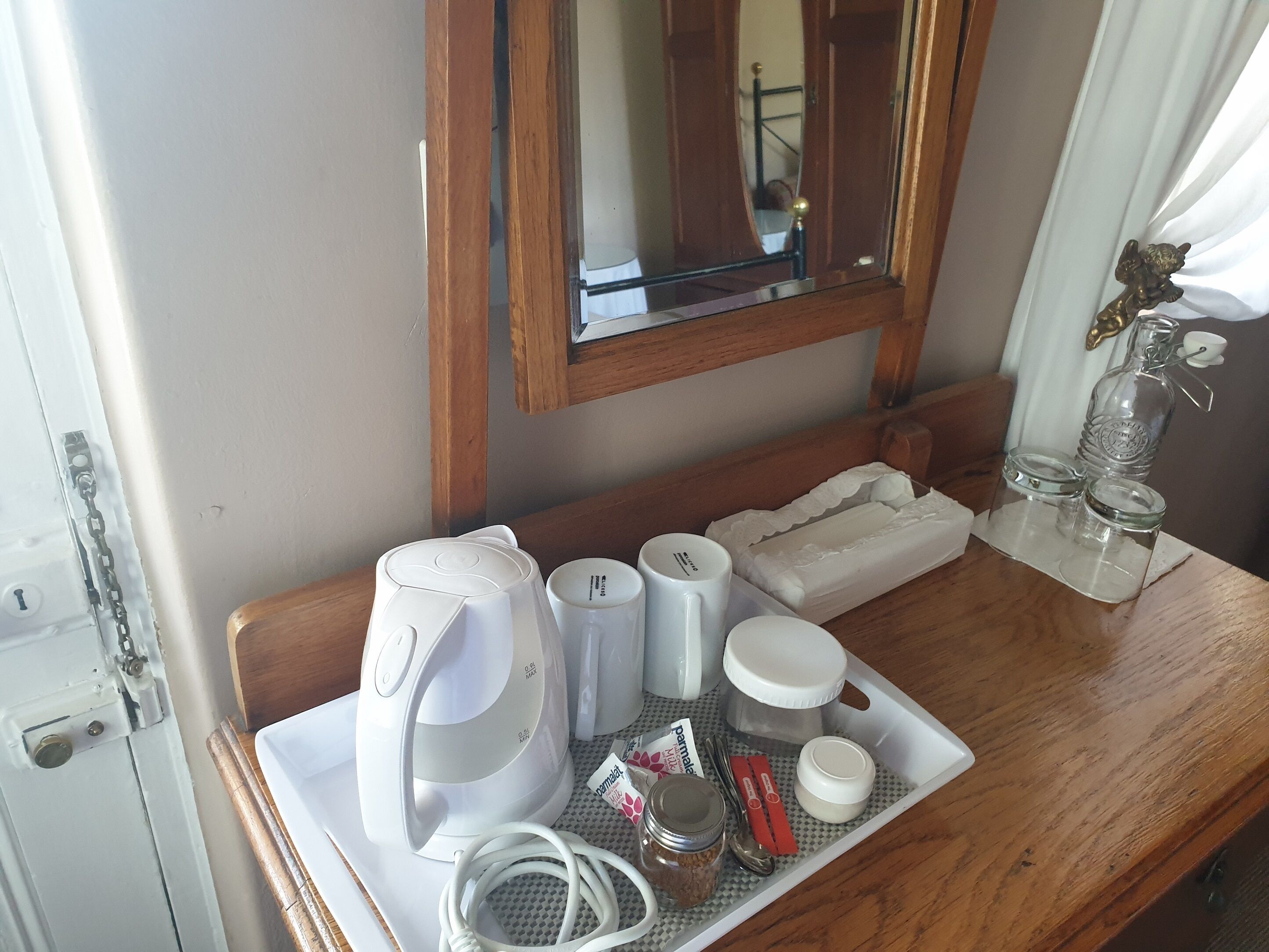 Hotelkamer met een houten kaptafel, een spiegel, een dienblad met een koffiezetapparaat, kopjes, een pot jam en een waterfles.
