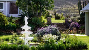 A garden with a white fountain, lush greenery, and a stone wall. - Zuurberg Mountain Village (Addo)