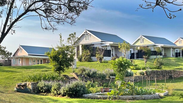 A residential area with multiple houses, a well-maintained lawn, and a stone wall. - Zuurberg Mountain Village (Addo)