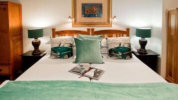 Una cama bien hecha con una manta verde, dos almohadas con estampados de autos, un cuadro enmarcado sobre la cama y dos lámparas de noche.