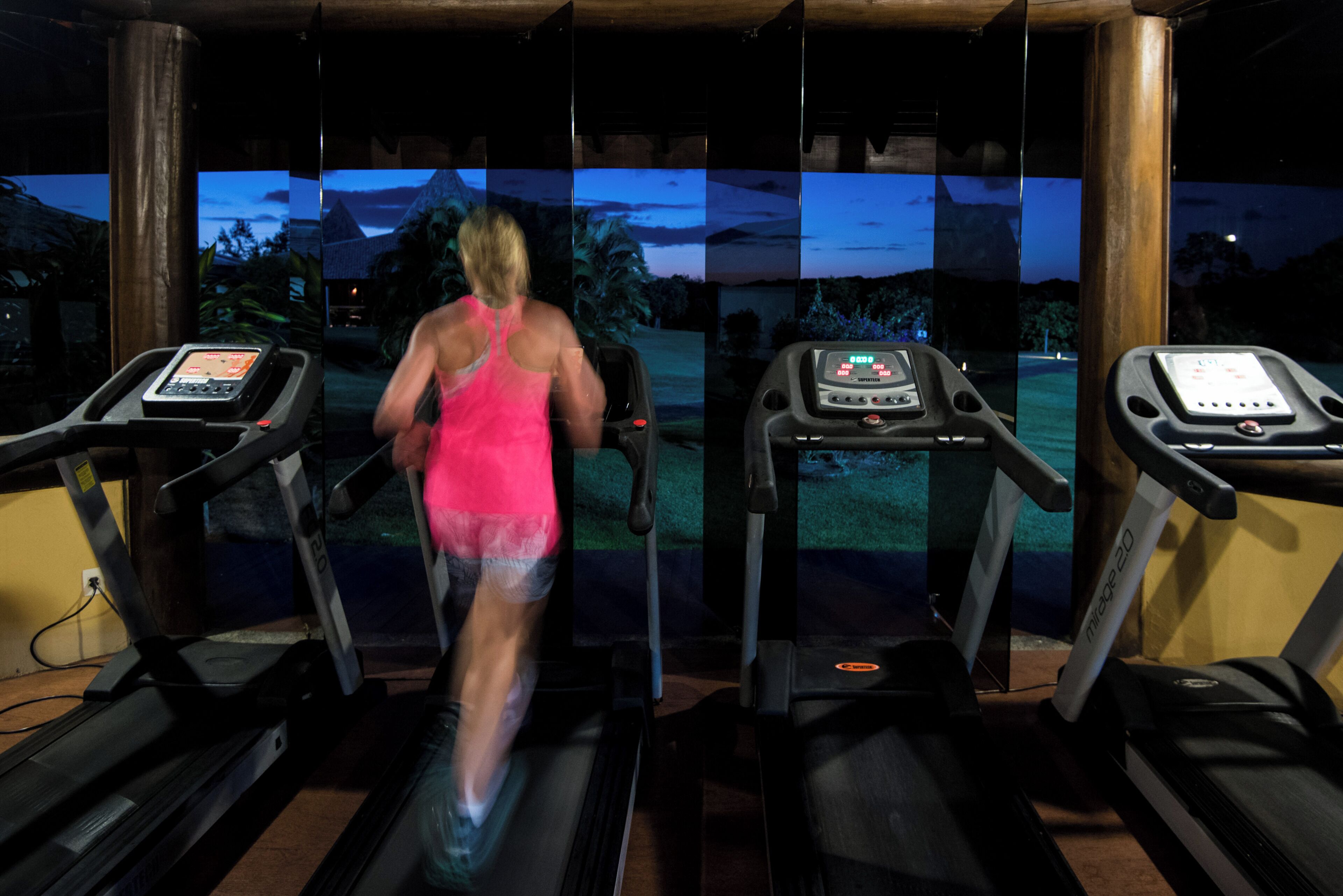 Una persona corriendo en una cinta de correr con una pantalla digital, en una habitación con un muro de vidrio.