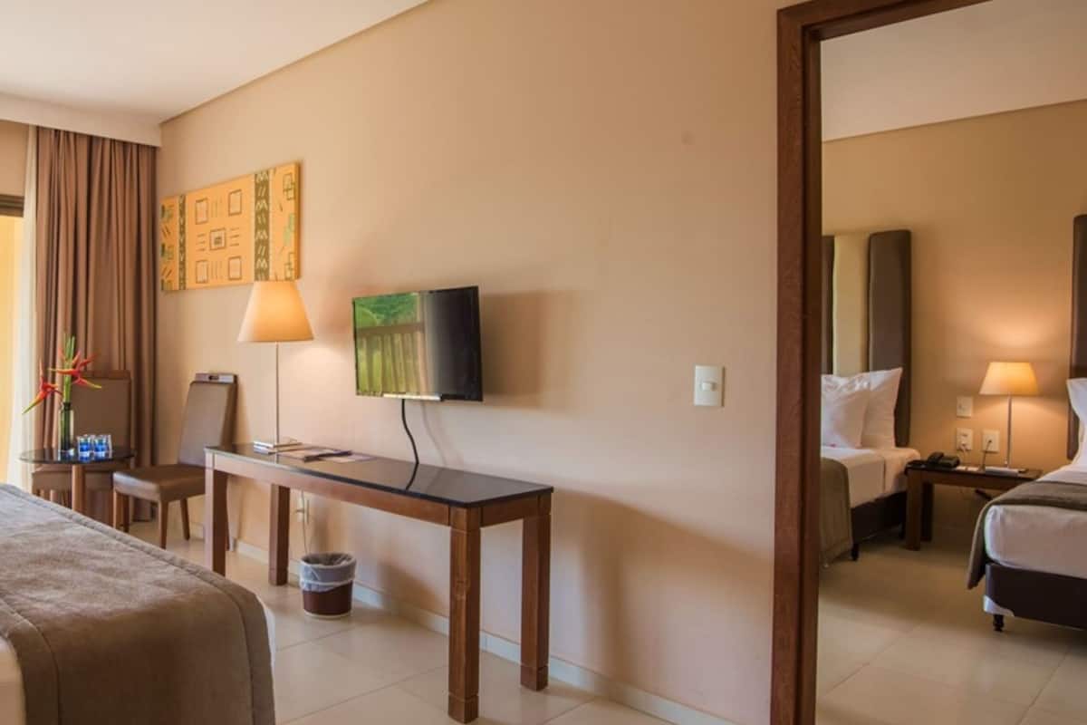 A hotel room with a bed, a desk, a chair, a TV, and a balcony with curtains.
