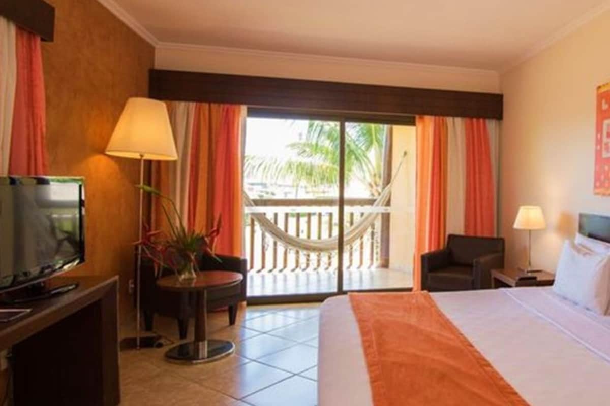 Habitación de hotel con cama, televisión, escritorio, silla, lámpara y vistas al exterior.