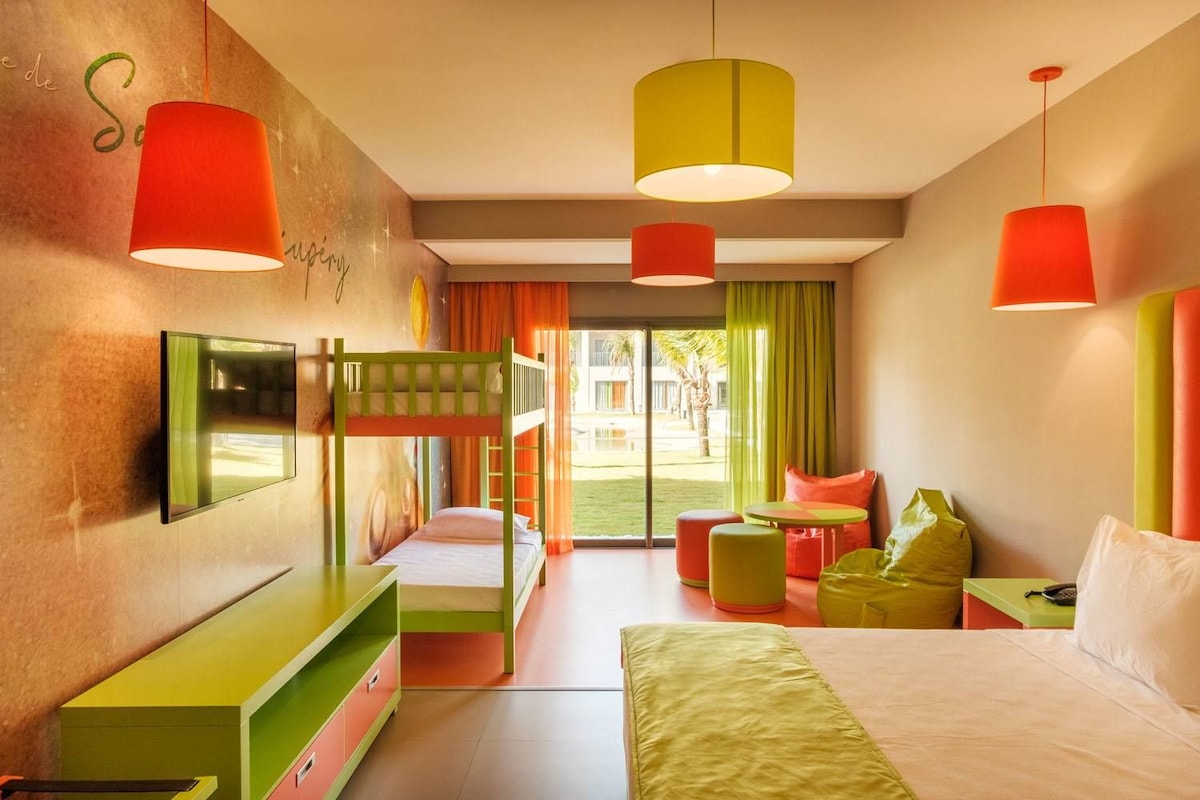 Habitación de hotel con literas, televisor de pantalla plana, cama con cubrecama verde y vistas al exterior.