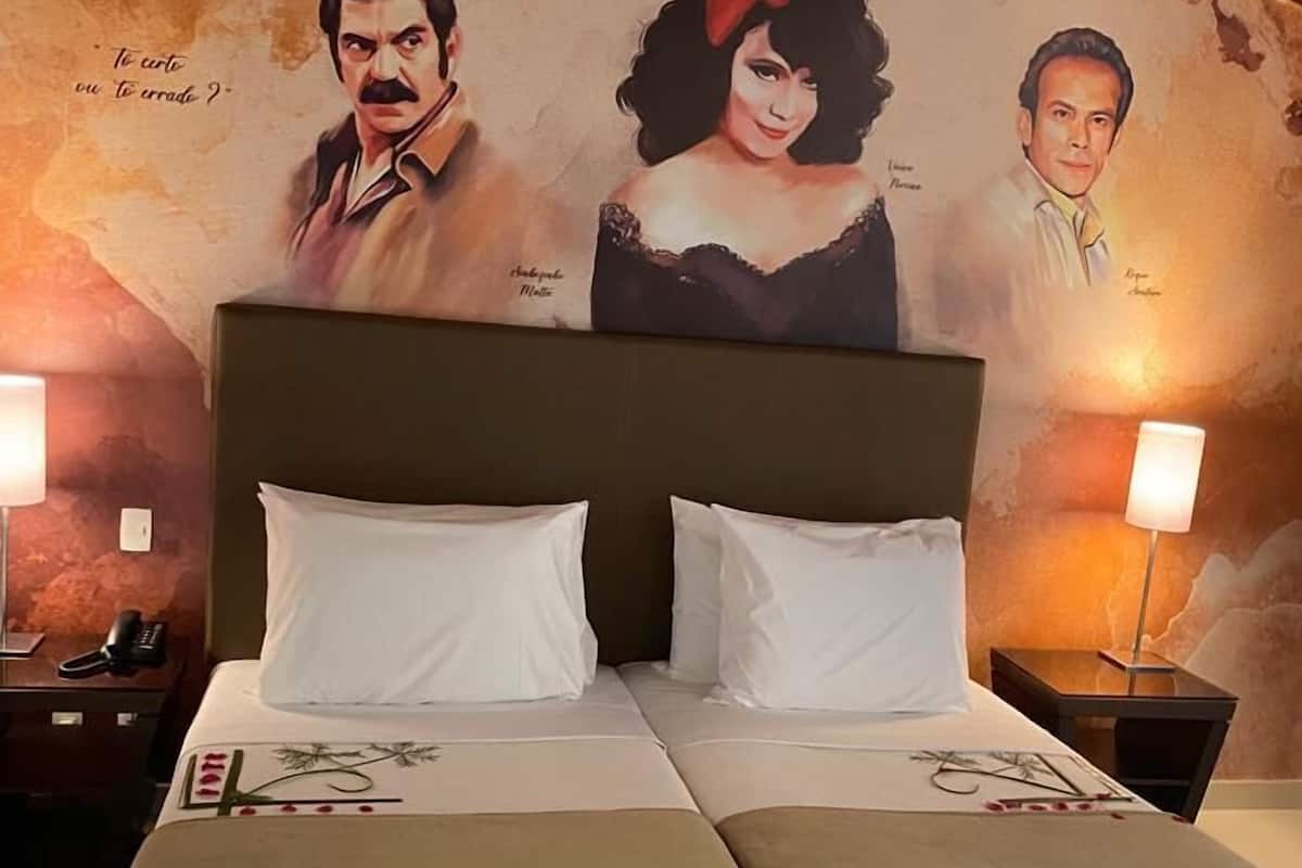 A double bed with white linens, two bedside tables, and a wall mural with portraits and text.
