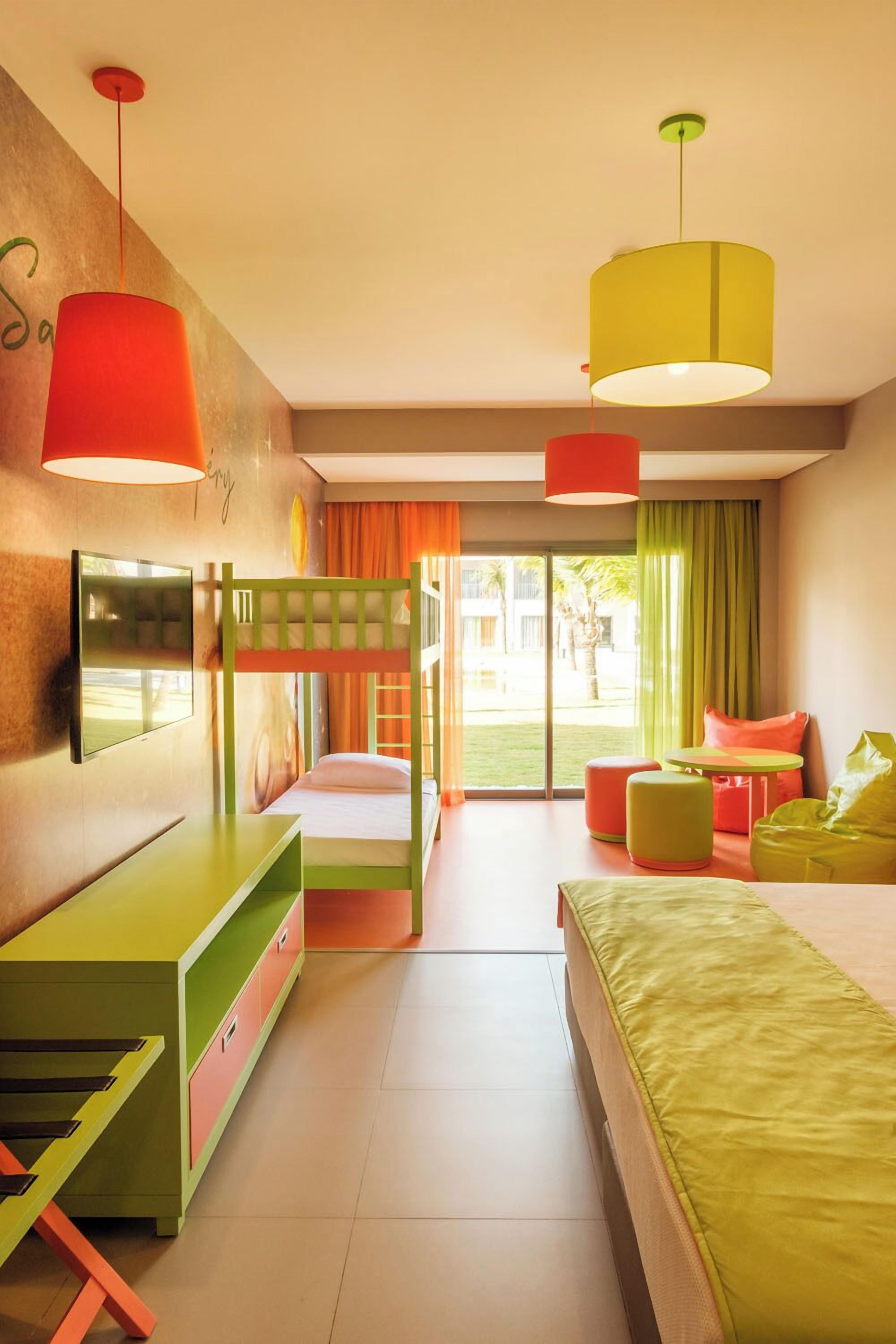 Ein helles Hotelzimmer mit Stockbetten, einem Fernseher, einem Schreibtisch und einem Fenster mit Blick ins Freie.