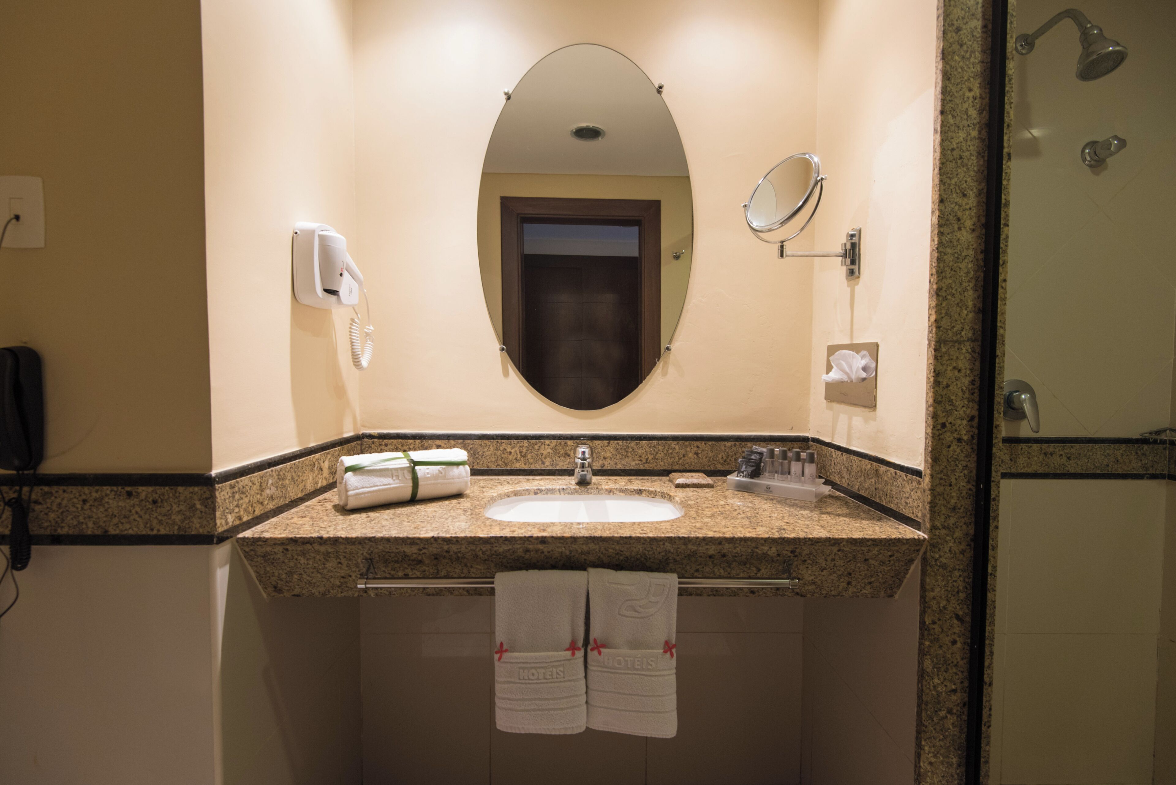 Ein Badezimmer in einem Hotel mit Waschbecken, Spiegel, Handtuchhalter und Duschbereich.