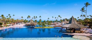 Zona de piscina en un resort, con palmeras, sillones de descanso y un bar.