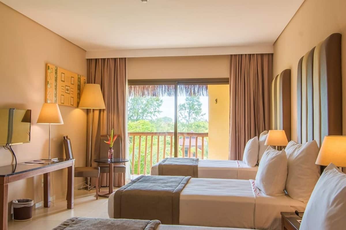 A hotel room with a bed, a desk, a chair, a small table, and a balcony with curtains.