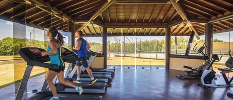 Un gimnasio con cintas de correr, bicicletas estáticas y techo cubierto.