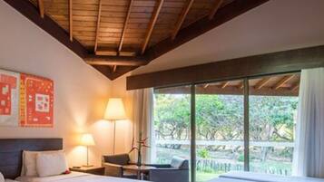 Habitación de hotel con cama, escritorio, silla y un amplio ventanal con vistas a árboles.