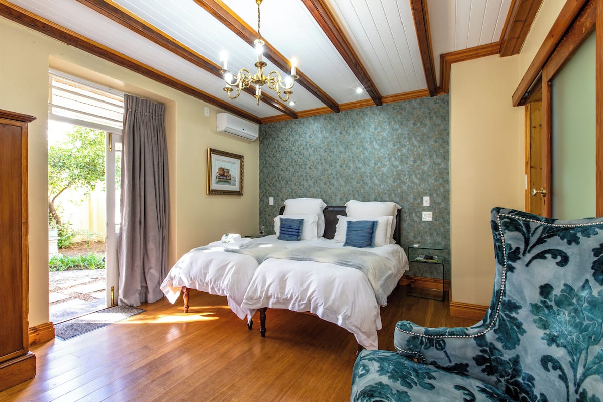 Ein Schlafzimmer mit Holzboden, einem Doppelbett mit weißer Bettwäsche, einem blauen Polsterstuhl und einer Kristallleuchter.