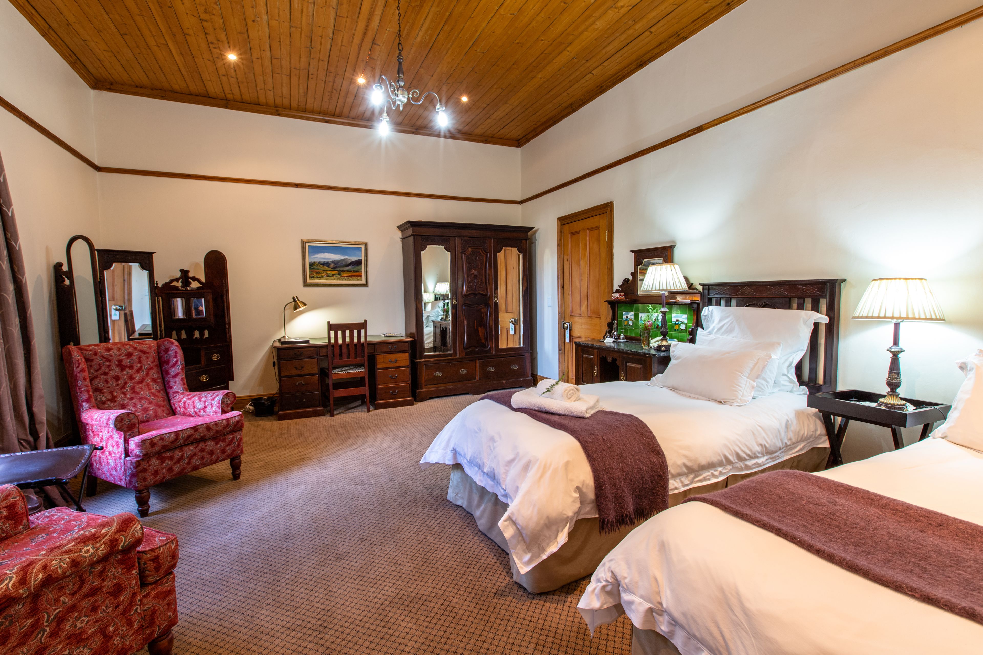 A hotel room with two beds, a wooden ceiling, a large mirror, a dresser, a chair, and a lamp.