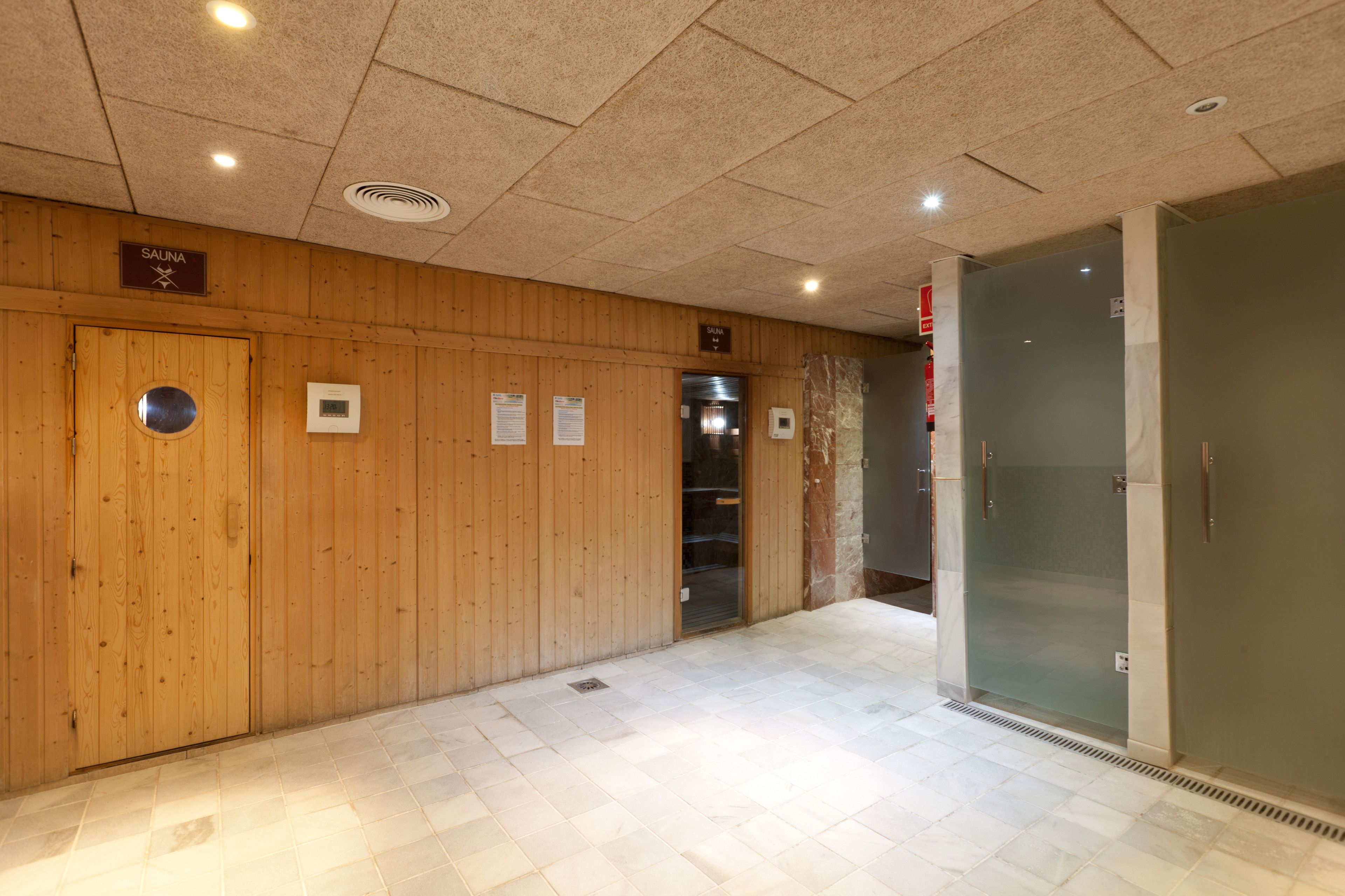 A wooden wall with a sauna sign, a glass door, and a tiled floor.