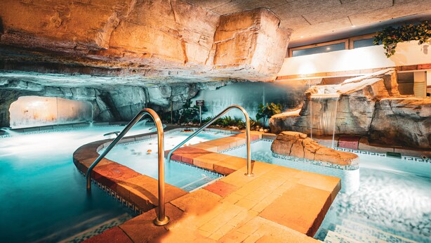 An indoor swimming pool with a rock wall backdrop, a waterfall feature, and a small waterfall. - Senator Cadiz Hotel (Cádiz)