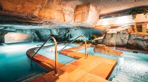 Una piscina interior con un muro de roca como fondo, una cascada y una pequeña cascada.