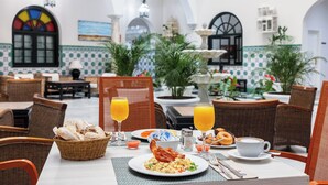 A dining area with wicker chairs, a table set with breakfast, including toast, eggs, bacon, and orange juice. - Senator Cadiz Hotel (Cádiz)
