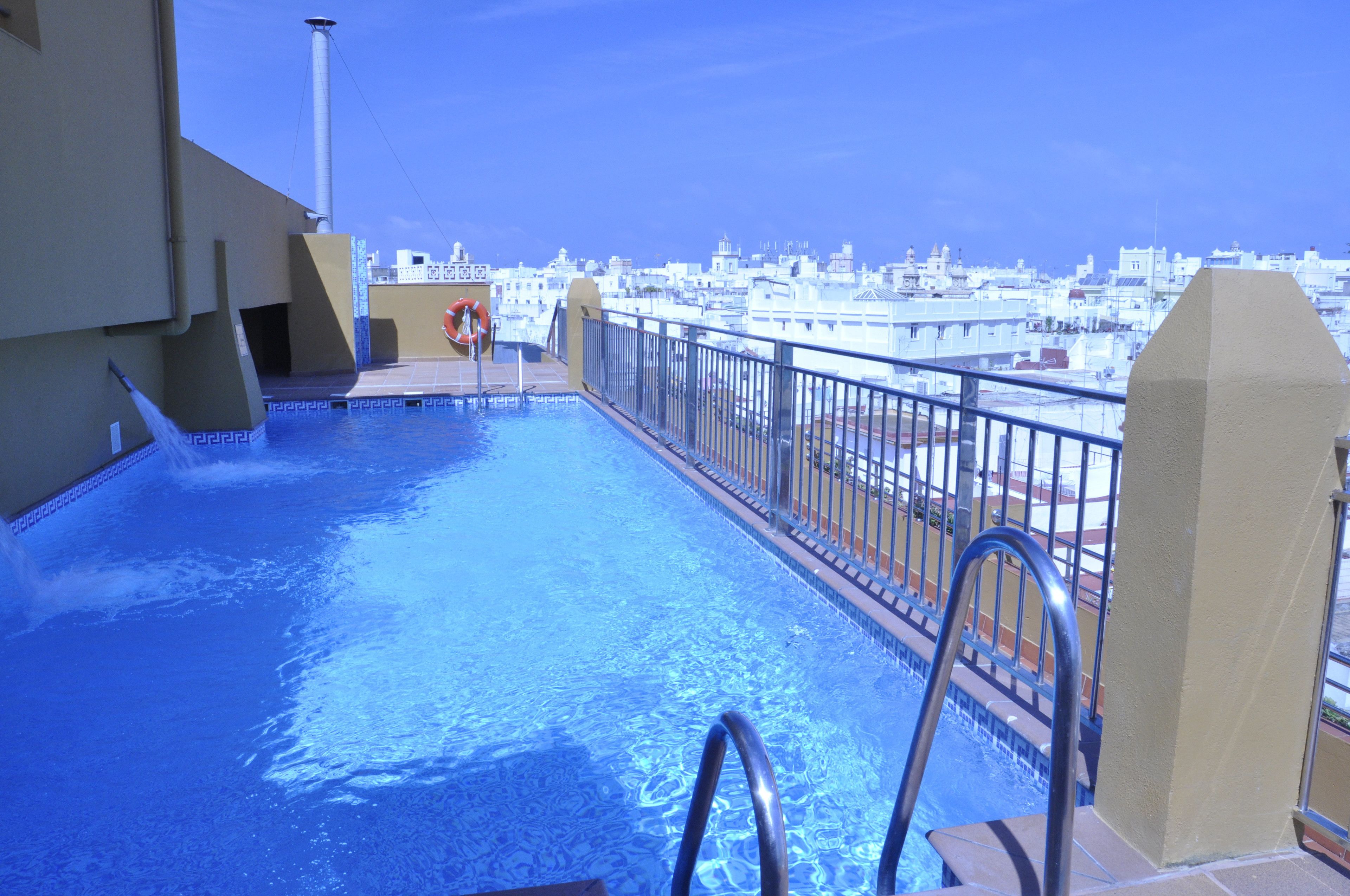 Piscina en la azotea con vistas a la ciudad, barandillas de metal y un flotador salvavidas.
