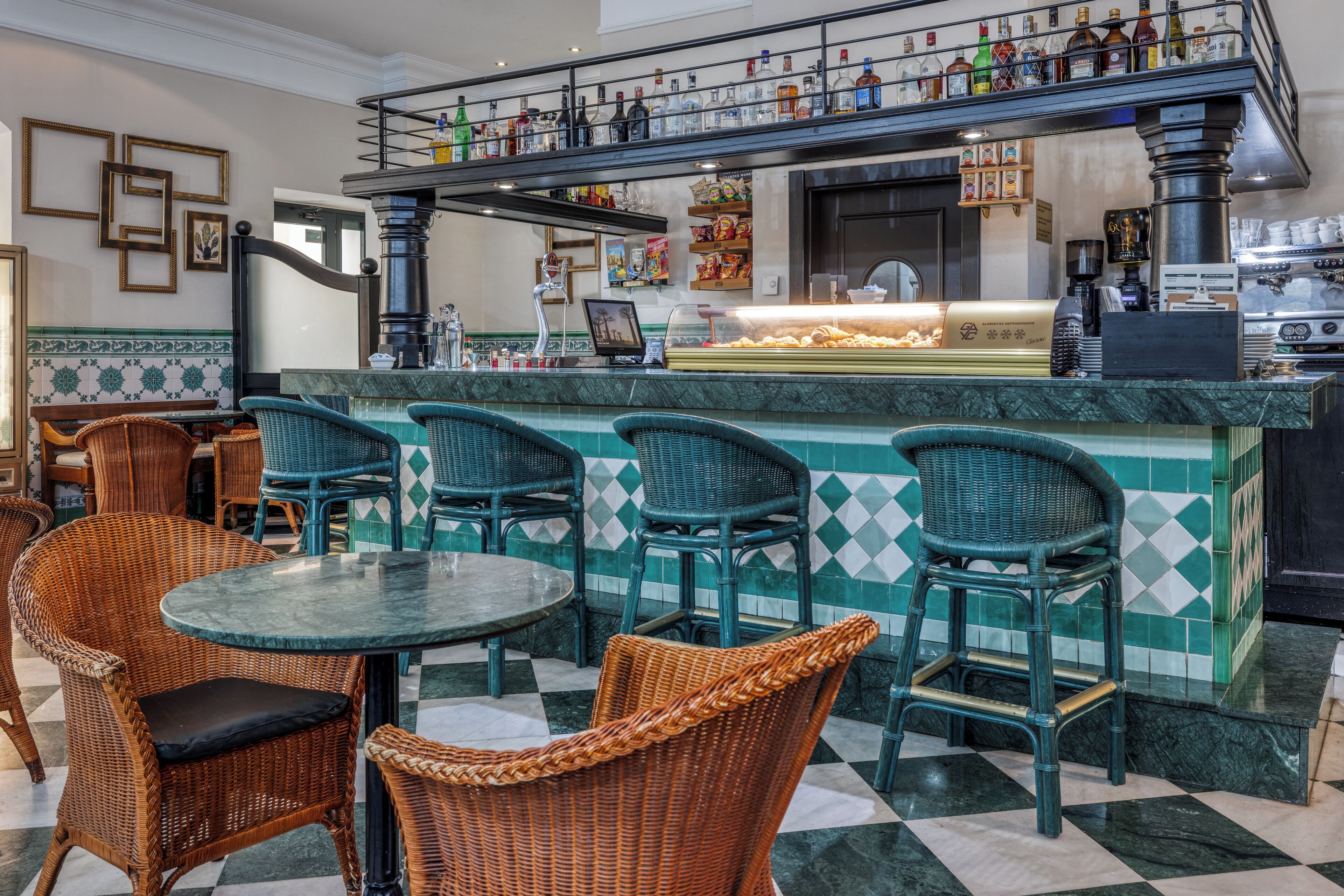 A bar area with wicker chairs and a counter displaying various bottles and snacks.