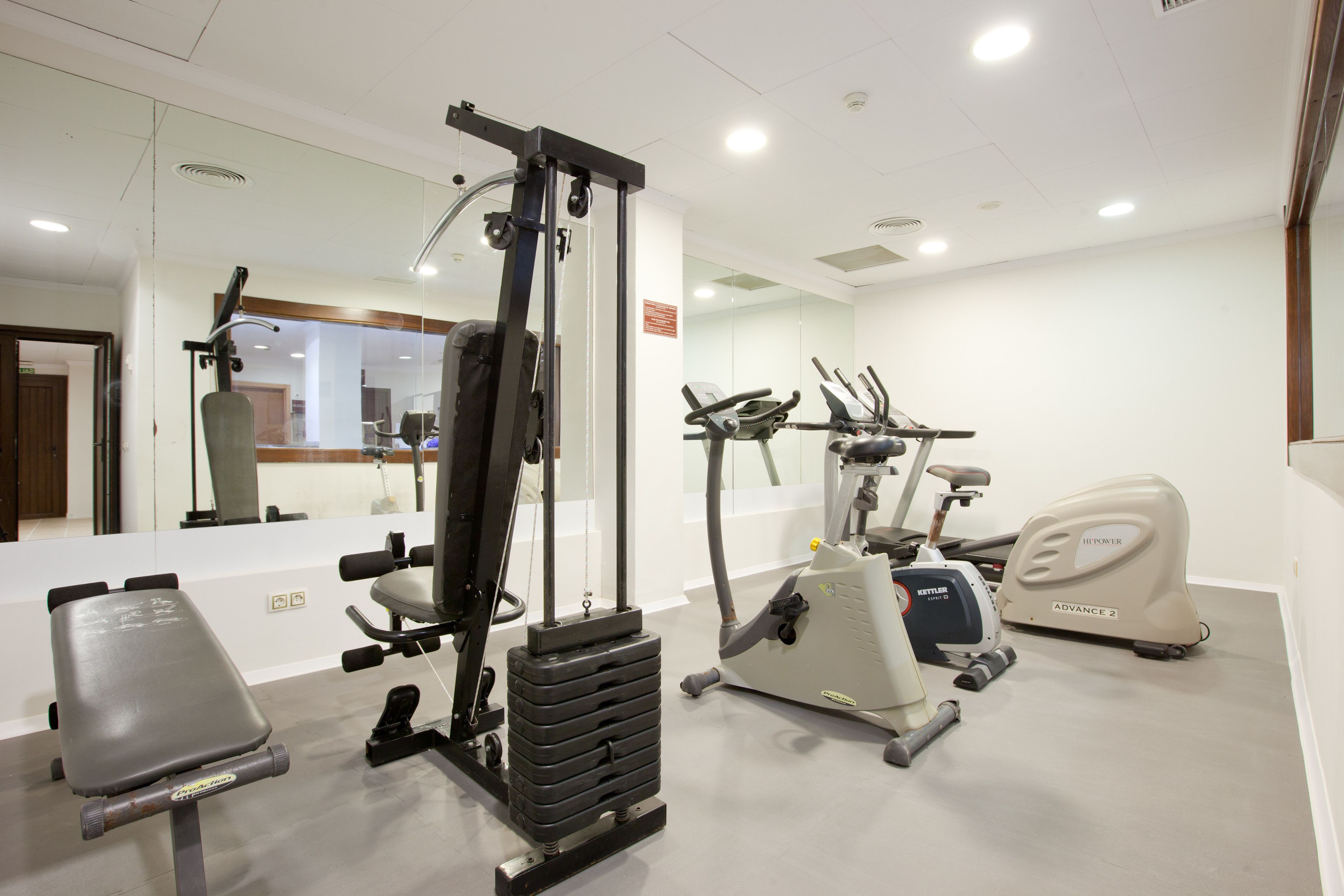 A gym with exercise equipment including a weight machine, a bench, and an elliptical.