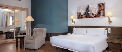 Habitación de hotel con una cama grande, una silla, un escritorio y un cuadro en la pared.
