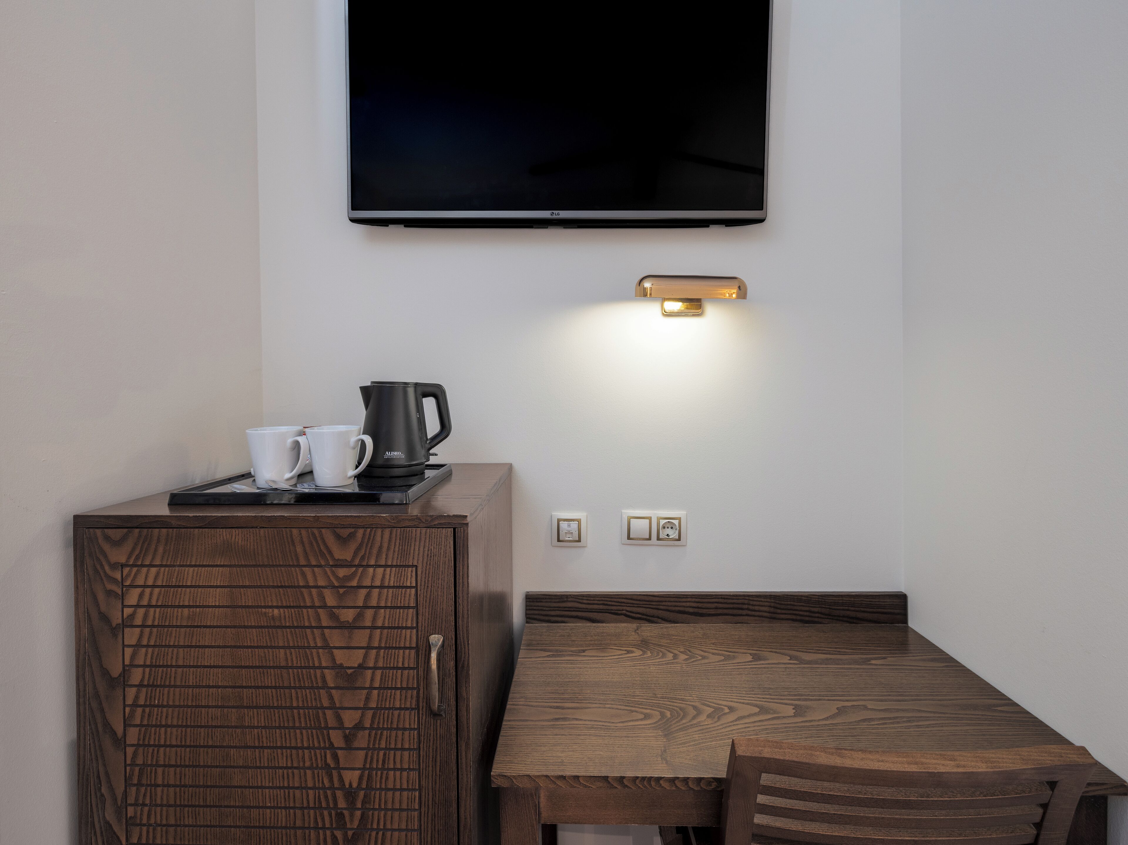 Habitació moderna amb televisió de pantalla plana penjada a la paret, un moble de vidre amb porta motllurada, una cafetera i una taula amb superfície de fusta.