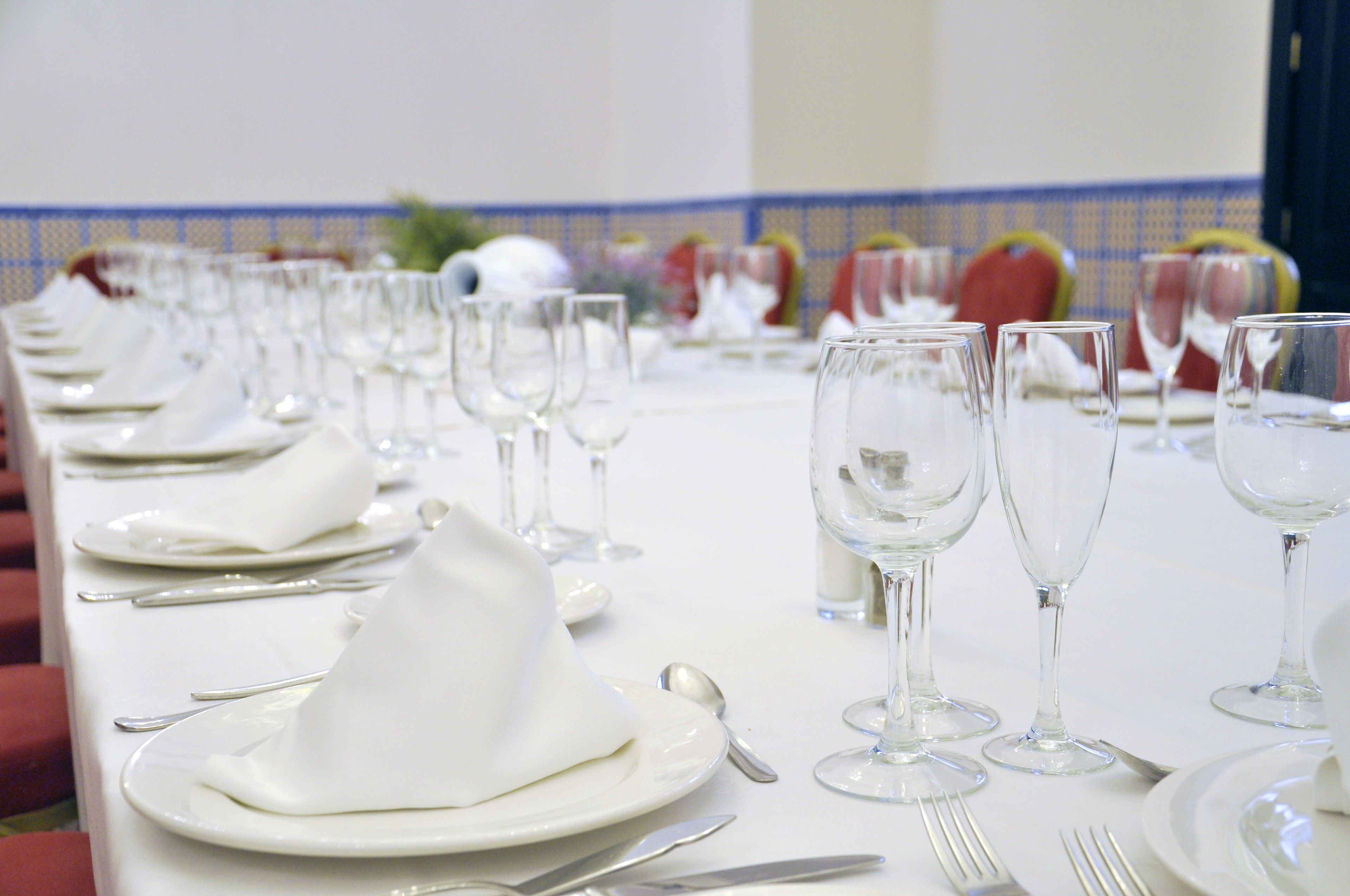A banquet table set with white tableware and wine glasses, indicating a formal dining arrangement.