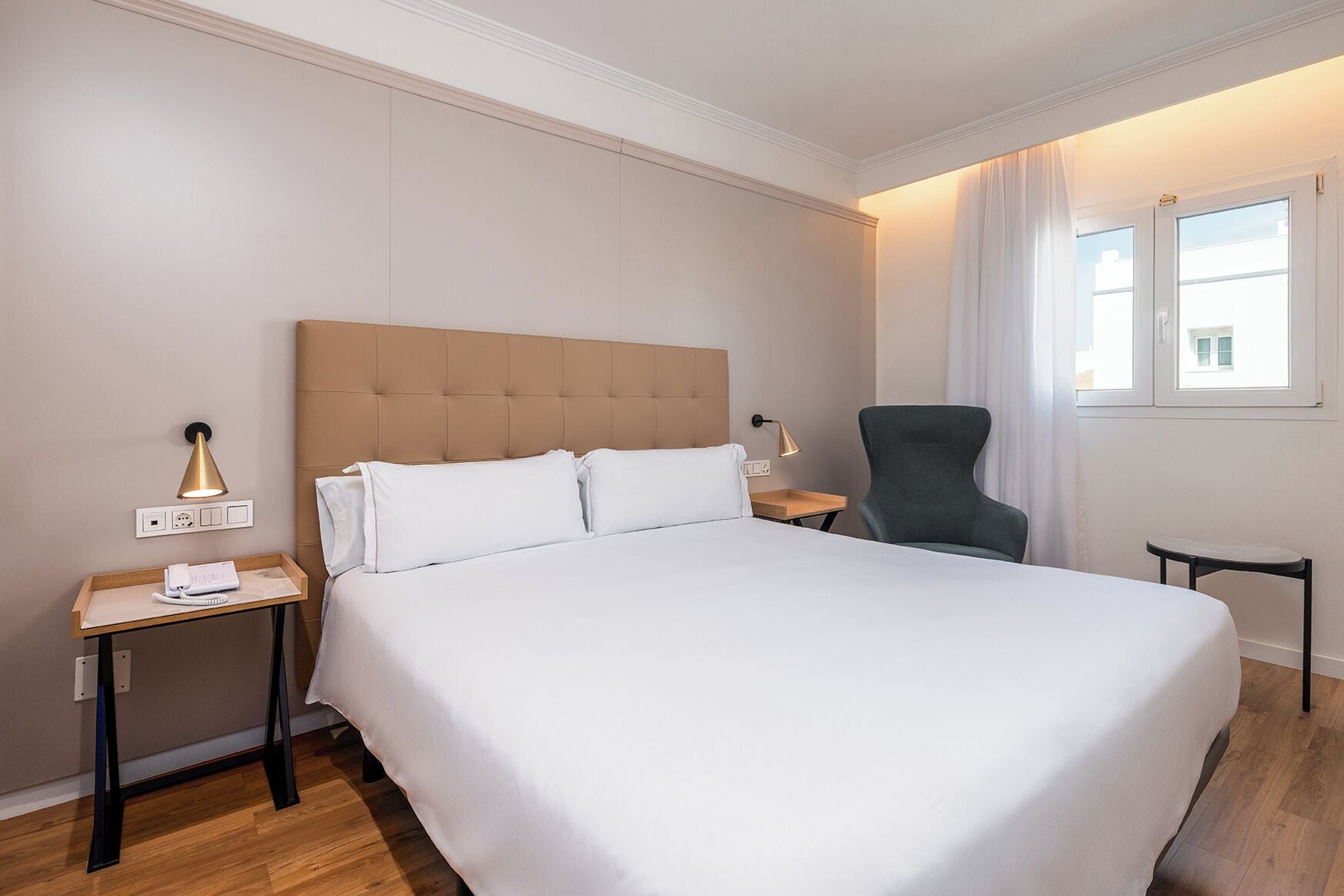 A hotel room with a large bed, a chair, a desk, and a window with curtains.