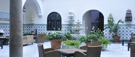 A spacious courtyard with a fountain, wicker furniture, and potted plants.