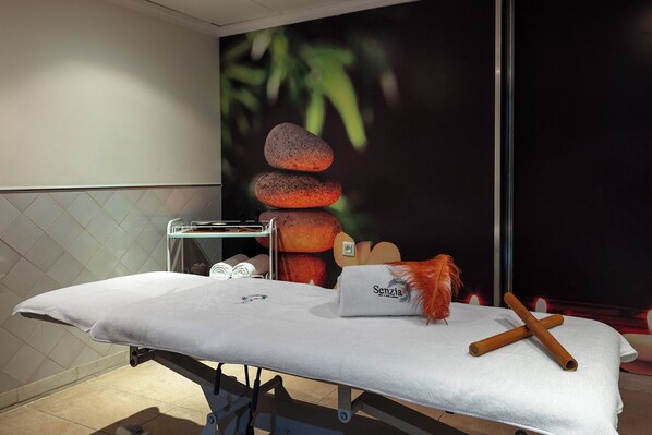 Mesa de masaje con toallas, un plumero y utensilios de madera en un entorno de spa.